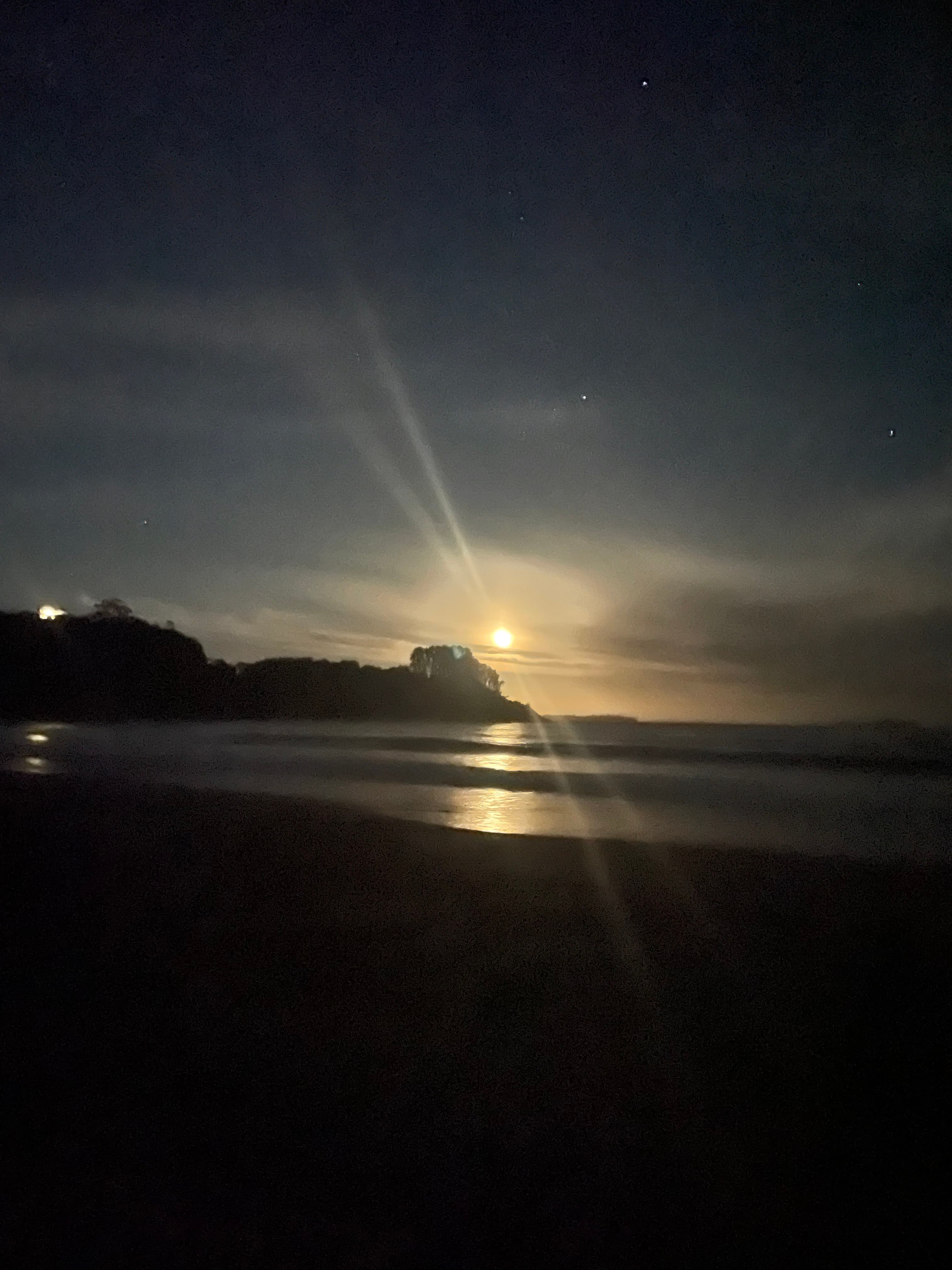 Bright moon shining over a dark coastline, casting long reflections on the calm night sea.